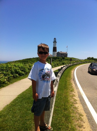 boy standing at road edge with Montauk lighthouse in foreground, Long Island, New York