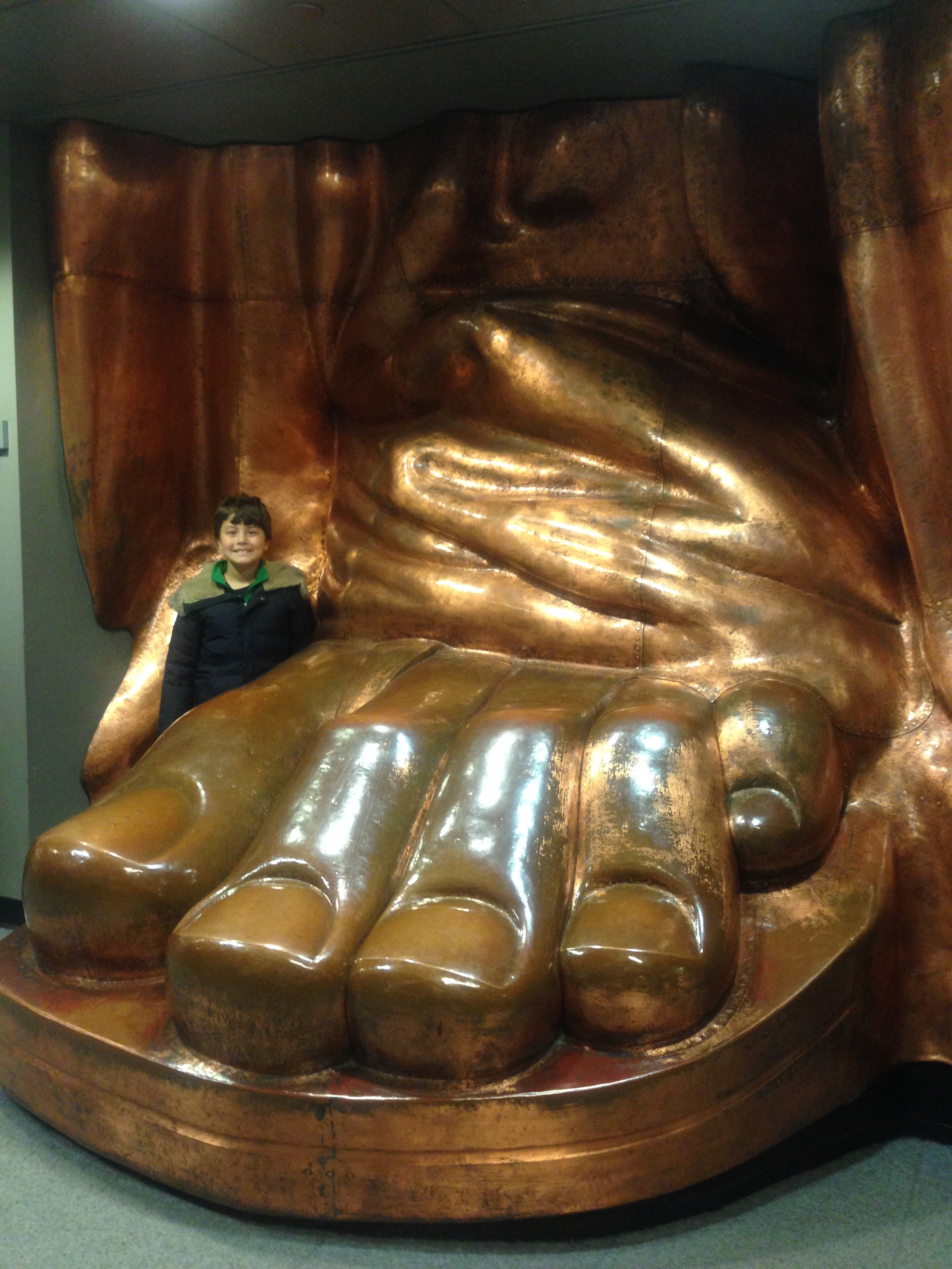 Boy posing next to museum sculpture of Statue of Liberty's foot, New York