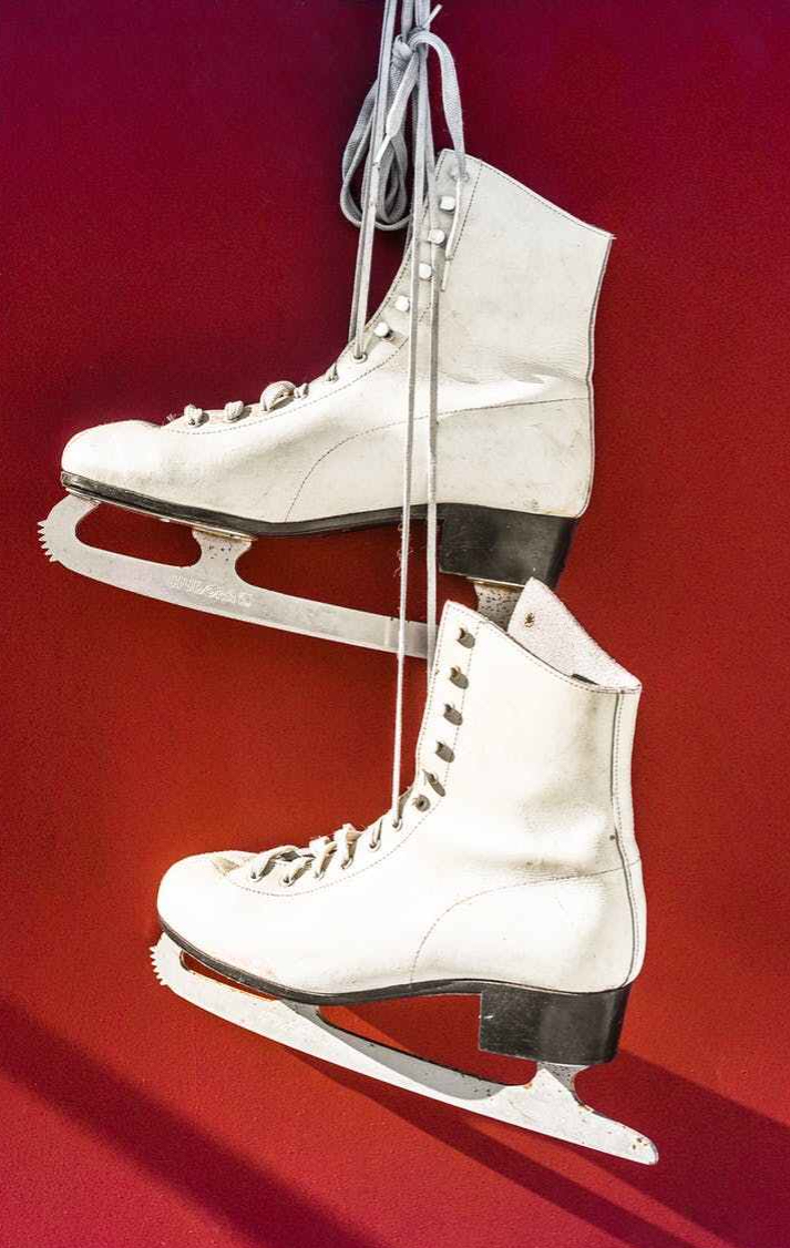 pair of white ice skates hanging against a red backdrop
